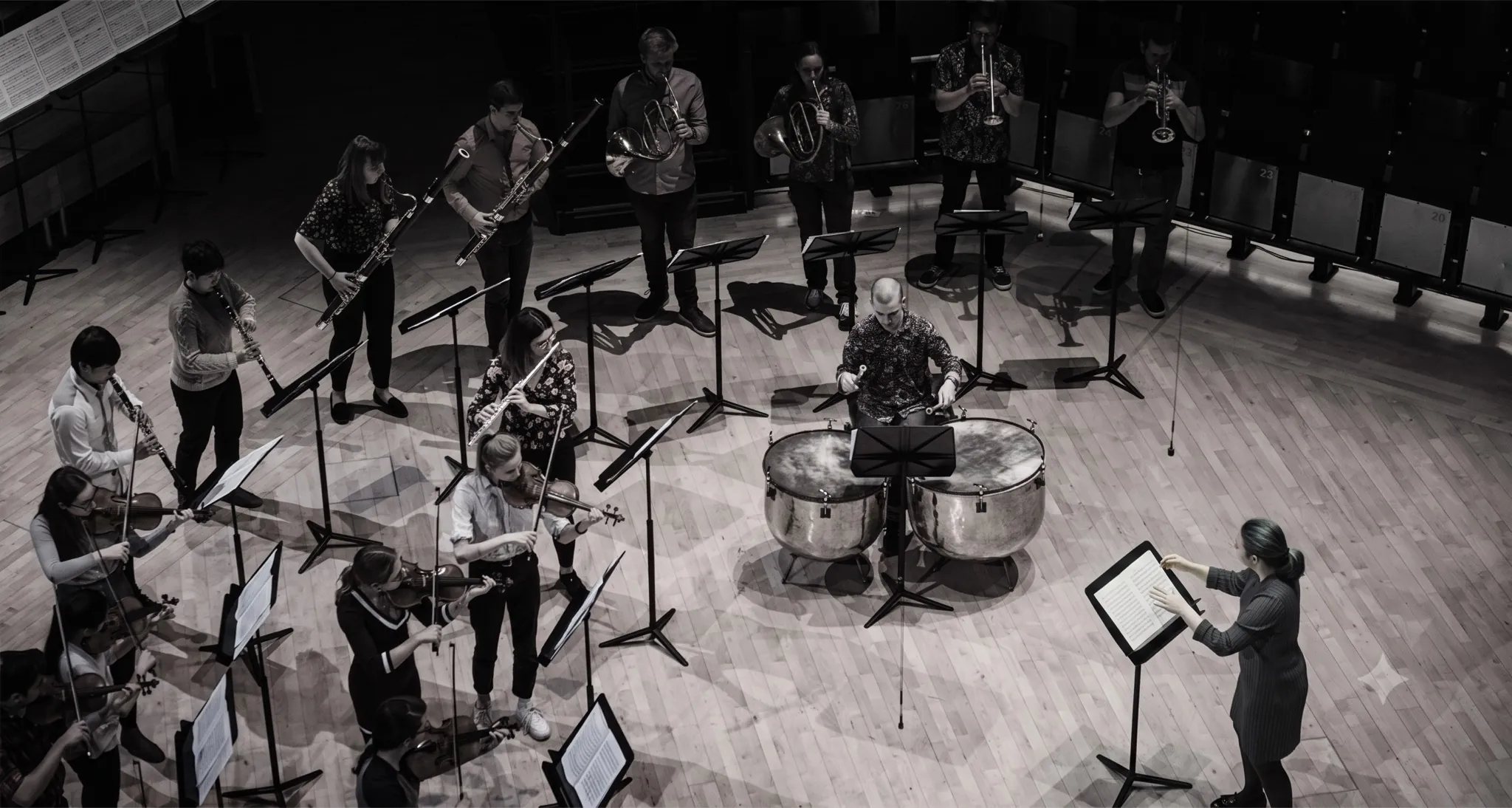 An orchestra rehearsing on a wooden stage, every musician following a conductor at the podium